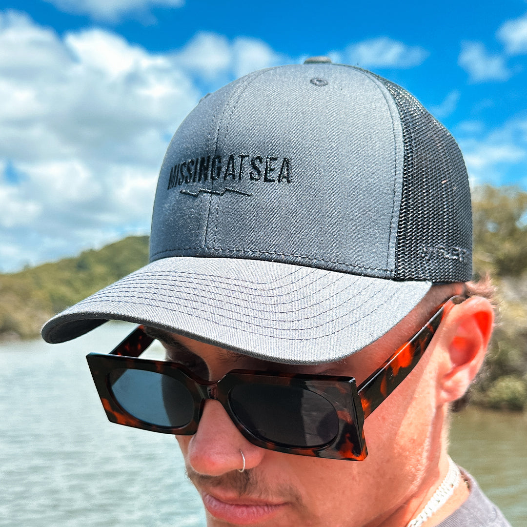 charcoal grey and black trucker hat with black Missing At Sea embroidered logo