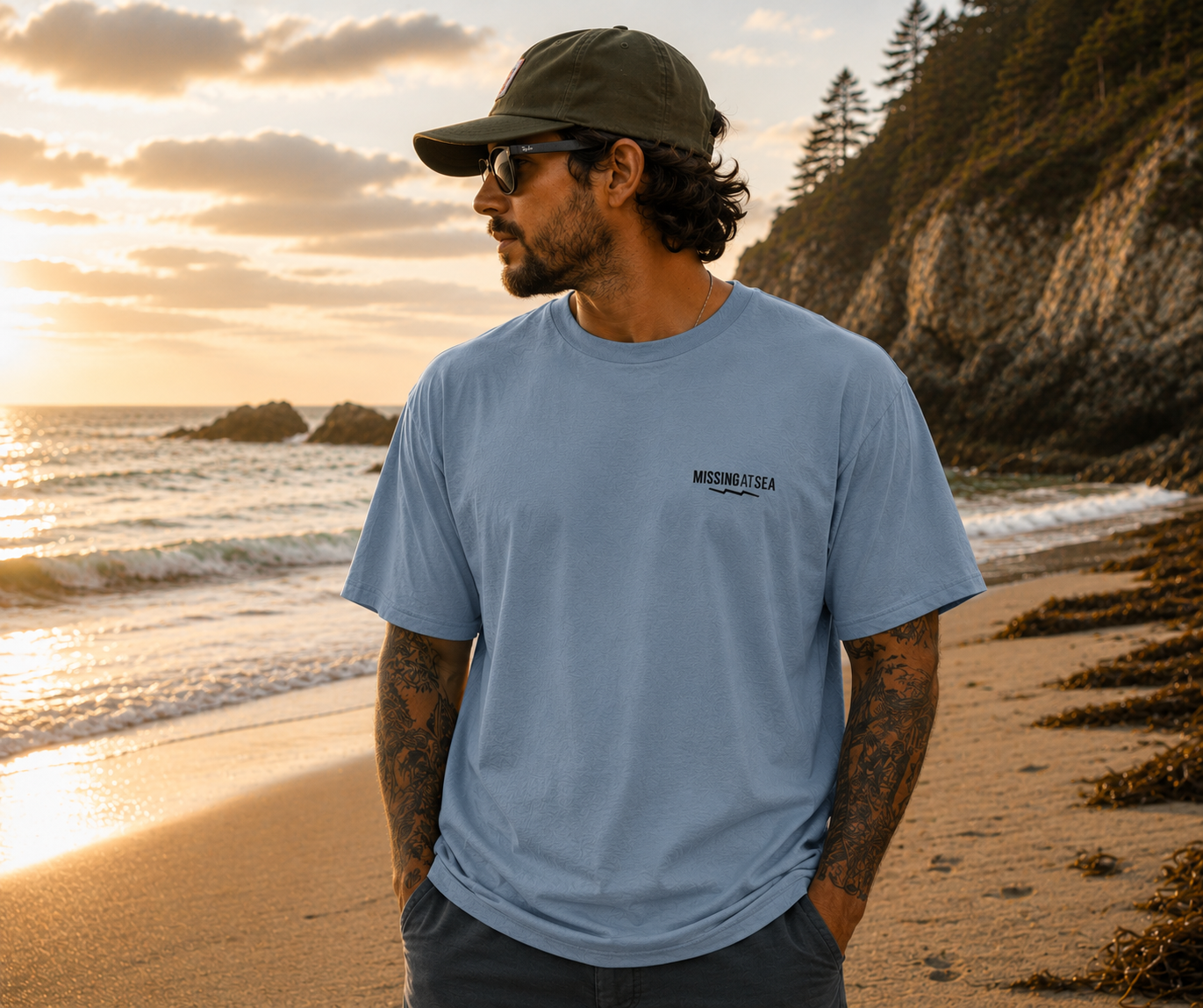 Man wearing a blue t-shirt with a logo on a beach at sunset