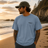 Man wearing a blue t-shirt with a logo on a beach at sunset
