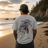 Man standing on a beach at sunset wearing a t-shirt with fish design