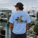 Man wearing a light blue t-shirt with fish graphics by a marina.