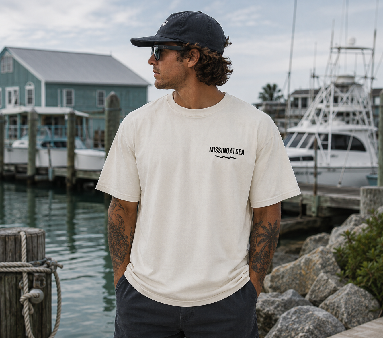 Man wearing a 'Missing at Sea' t-shirt by a marina with boats and houses in the background.