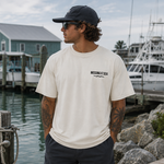 Man wearing a 'Missing at Sea' t-shirt by a marina with boats and houses in the background.
